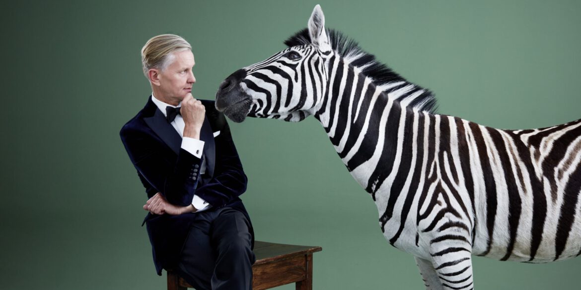 Max Raabe sitzt auf einem Tisch neben einem Zebra
